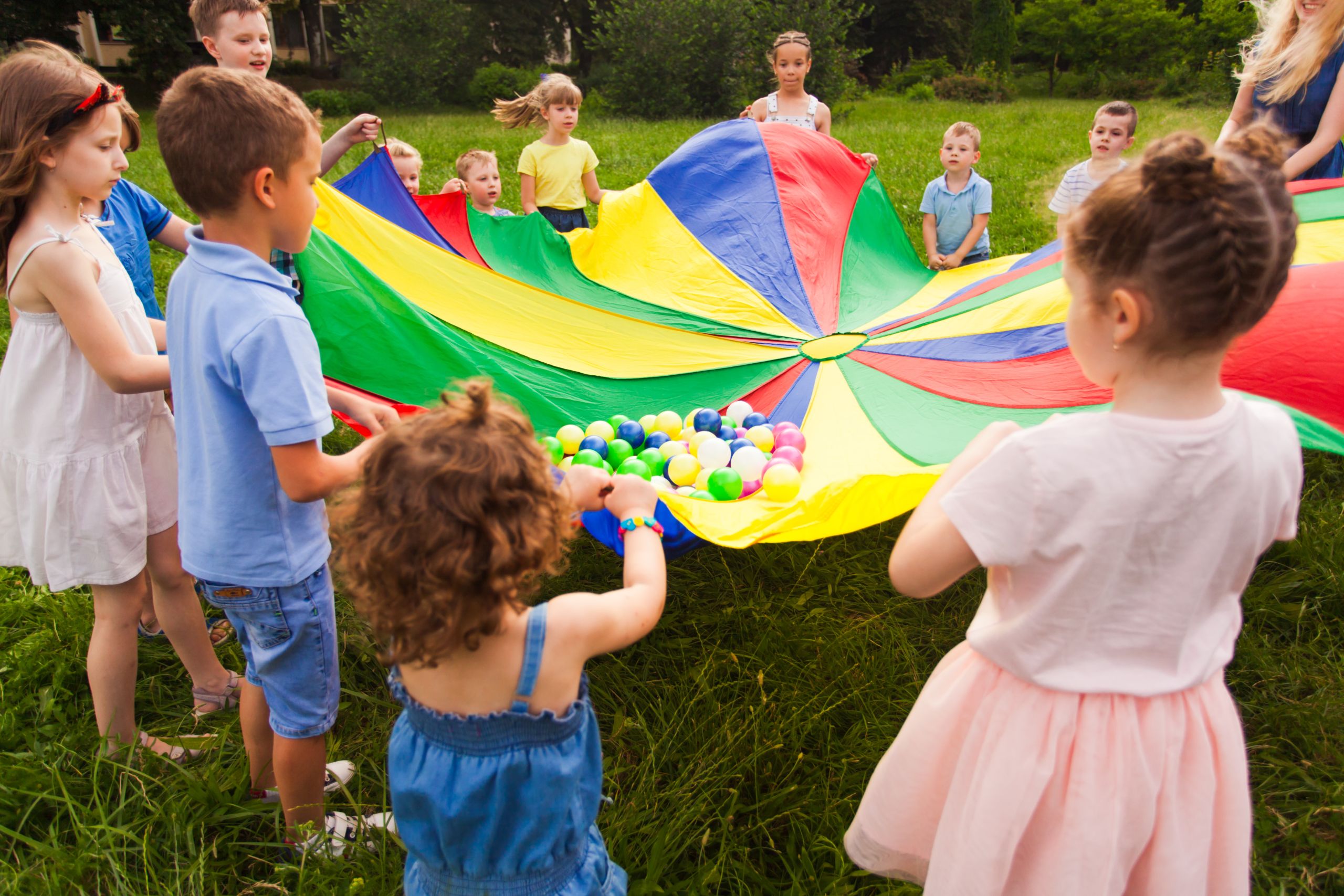 Close-up view kids of different age tightly holding colored parachute with small balls on it. Kids rolling over small balls on parachute, sending massage to each other. Good interconnection concept
