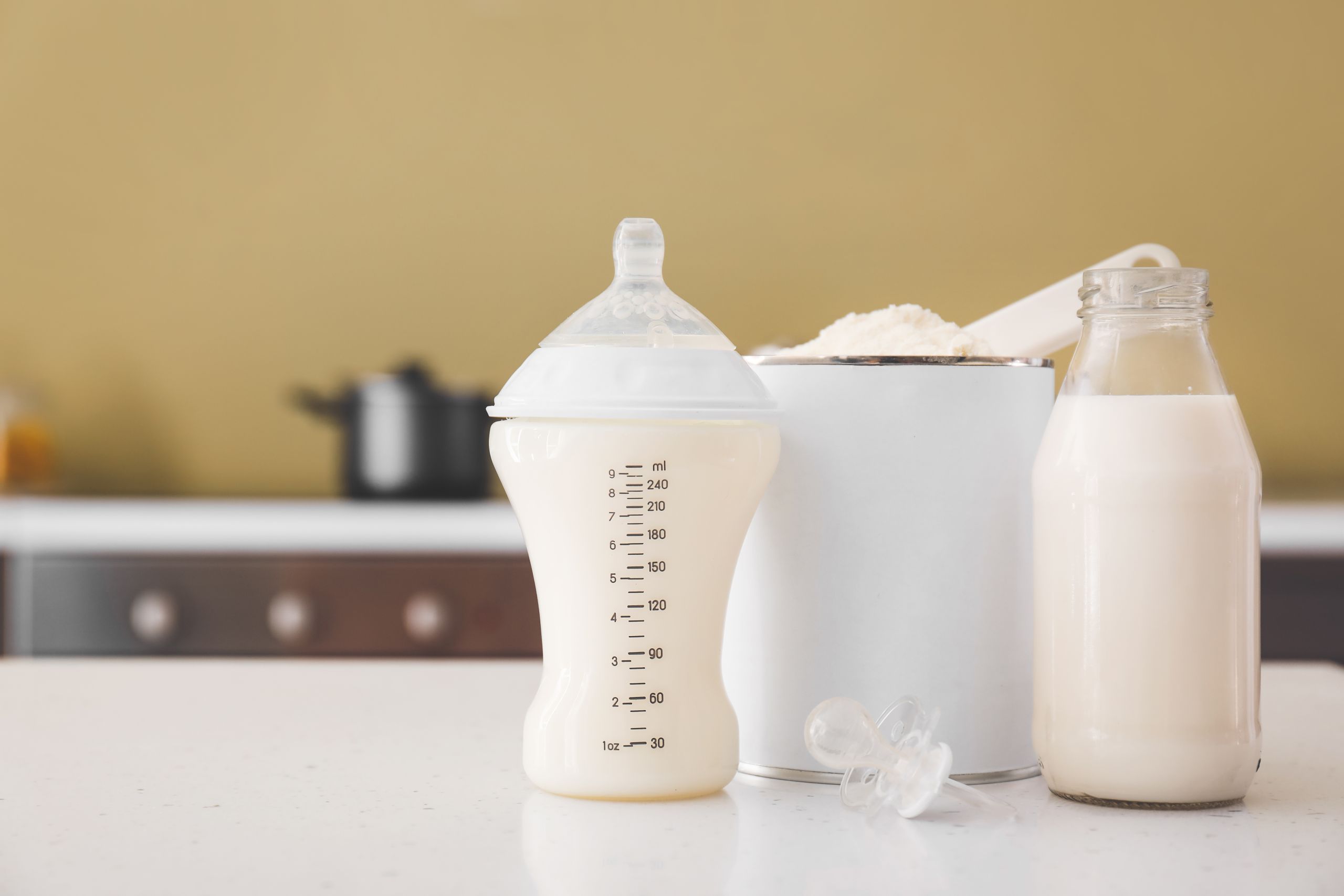 Bottles of milk and jar with baby formula on table in kitchen