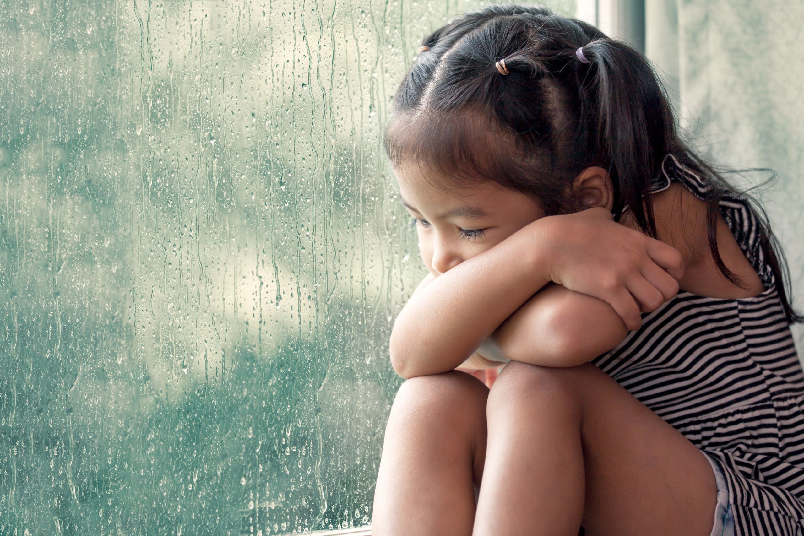 Sad asian little girl looking outside through the window in the rainy day in vintage color tone
