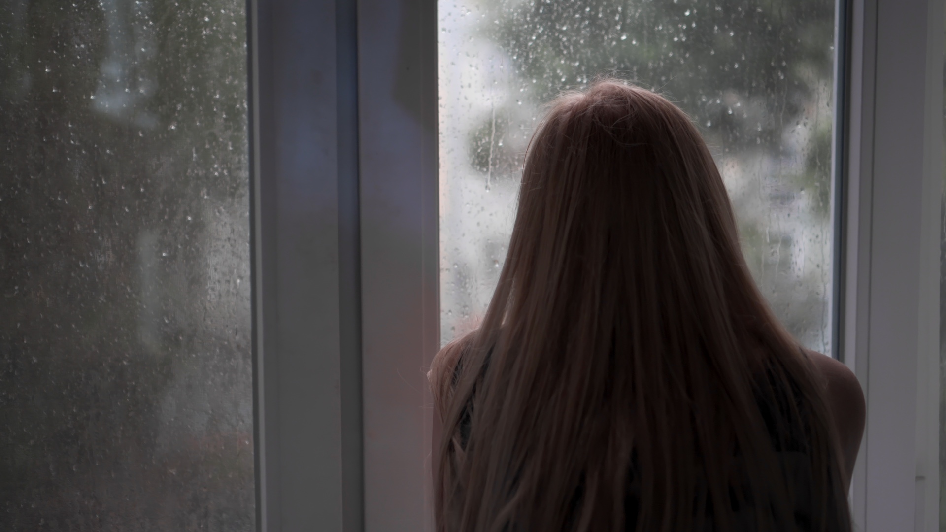 A woman looking out a rainy window experiencing seasonal depression